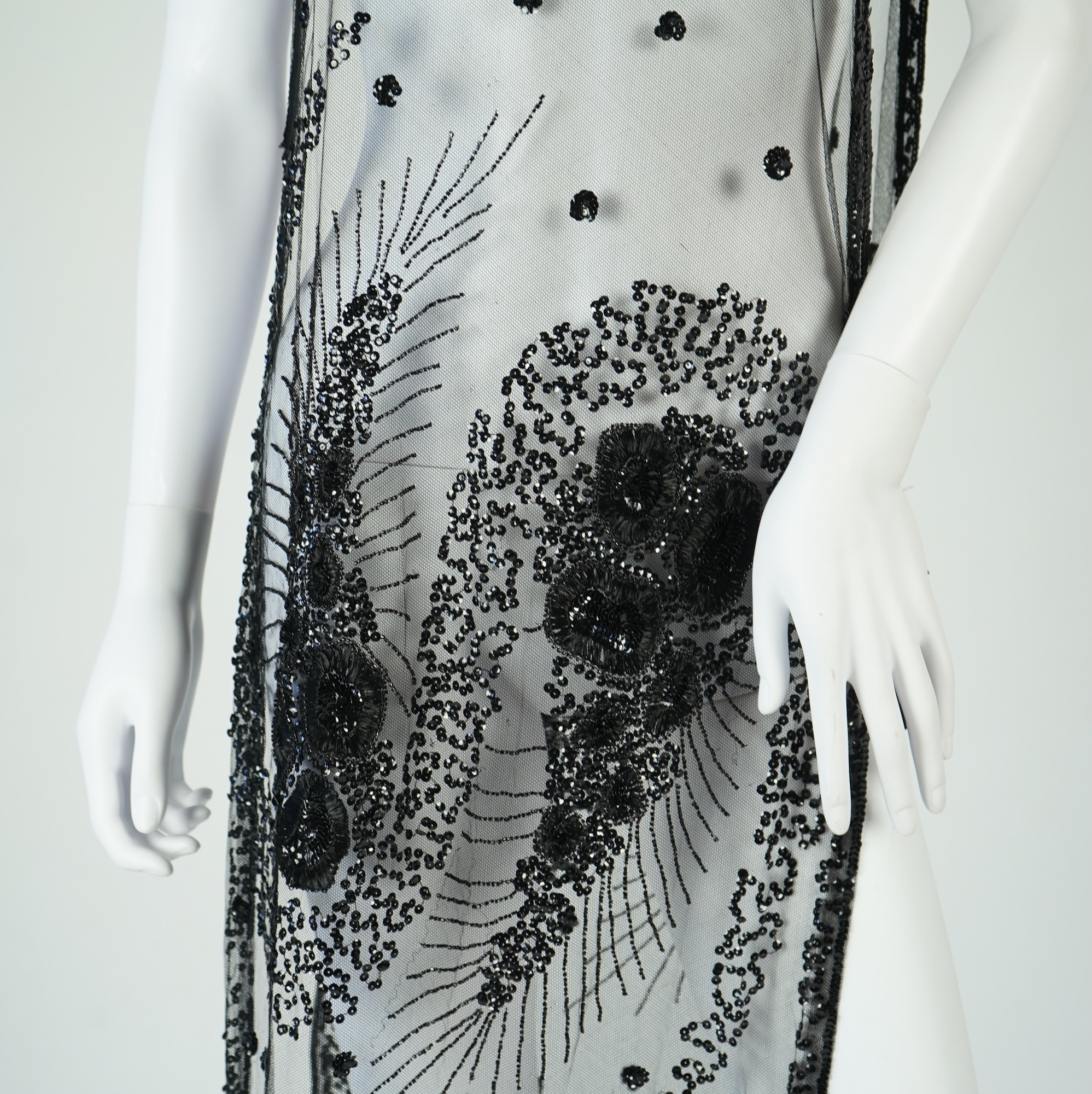 A 1920's black sequin on net tabard, with floral decoration and two side sequinned straps. Length 97cm. Condition - a few sequins have detached but are in a bag for re-attaching.